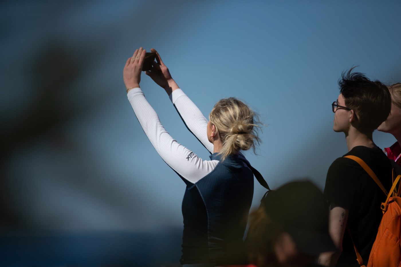 En ung kvinne holder mobilen oppe og tar bilde av en utsikt. En ung mann står bak og ser på utsikten.