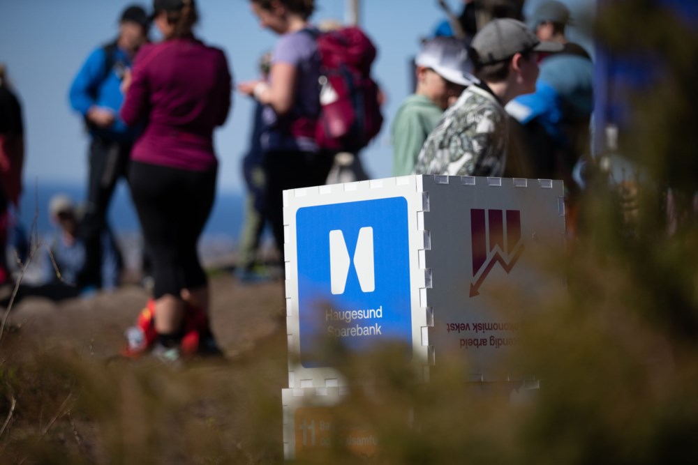 En boks med logoen til Haugesund Sparebank står på et fjell omgitt av turfolk