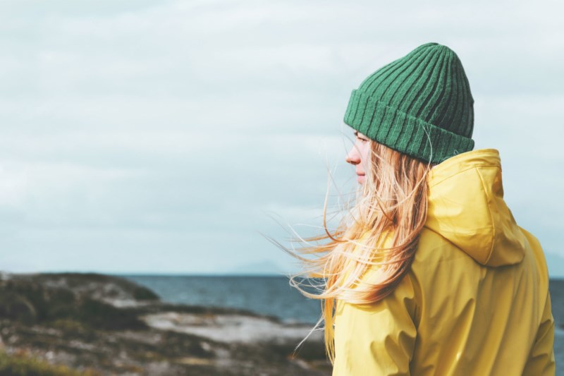 En dame i en gul regnjakke og med en grønn lue på hodet ser utover havgapet