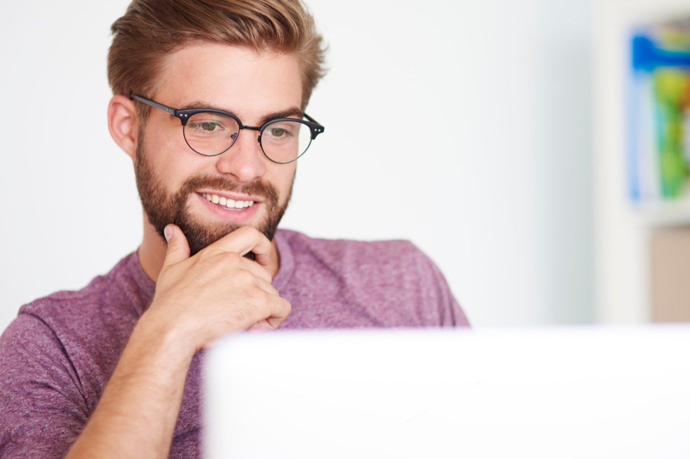 En mann smiler mens han ser på laptopen